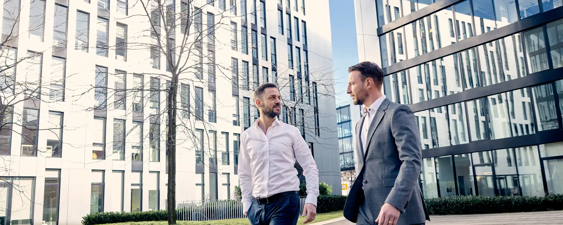Denis Drago und Christoph Enzenmüller von der Personalberatung head for work gehen im Gespräch nebeneinander her, im Hintergrund ist das Bürogebäude an der Johannstraße.