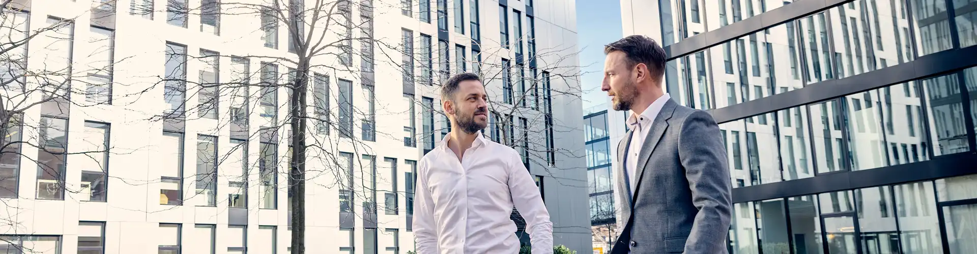 Denis Drago und Christoph Enzenmüller von der Personalberatung head for work gehen im Gespräch nebeneinander her, im Hintergrund ist das Bürogebäude an der Johannstraße.